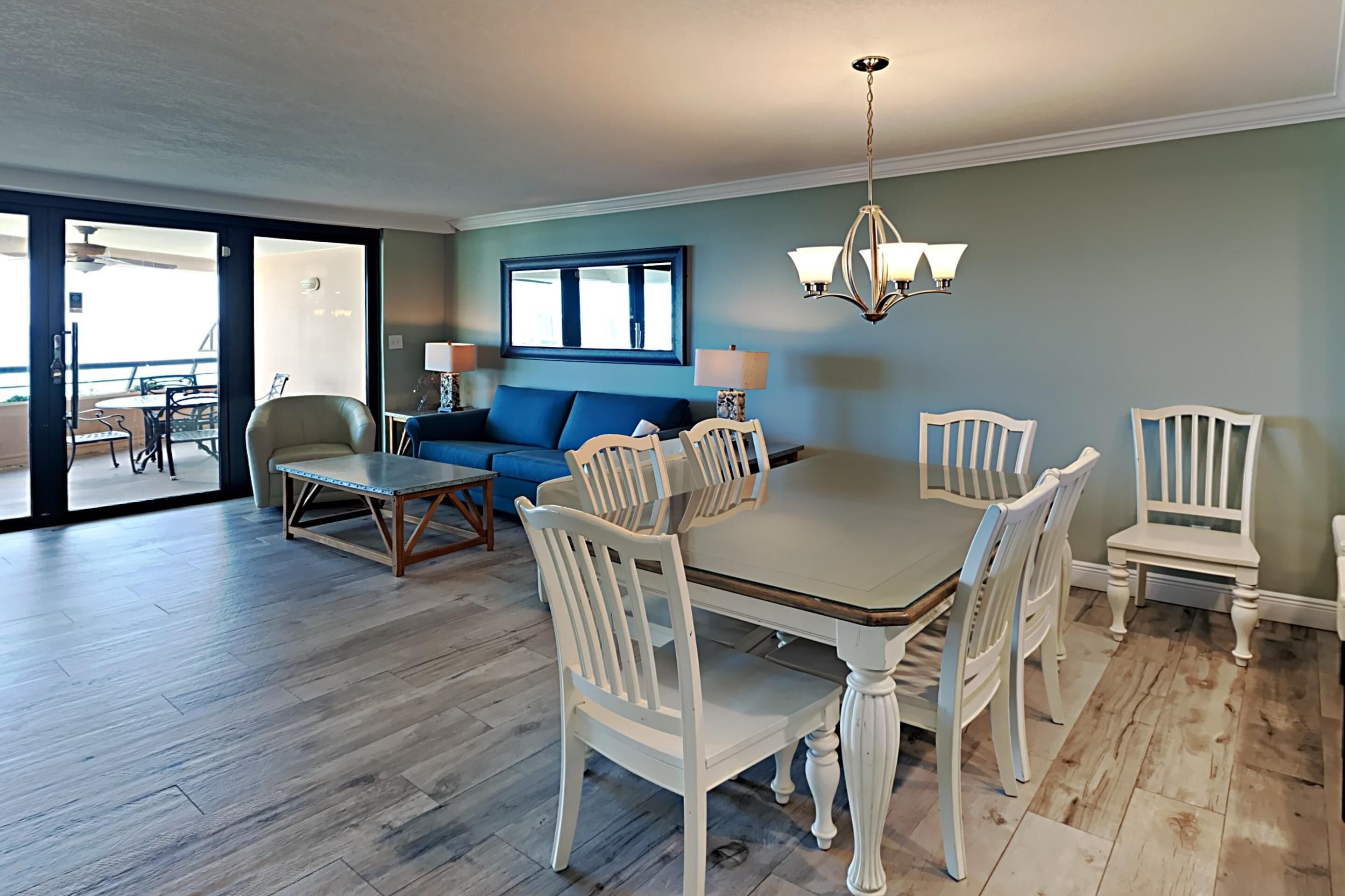 Ein Essbereich mit Holztisch und weißen Stühlen, einem blauen Sofa und einer Kristallleuchtre.