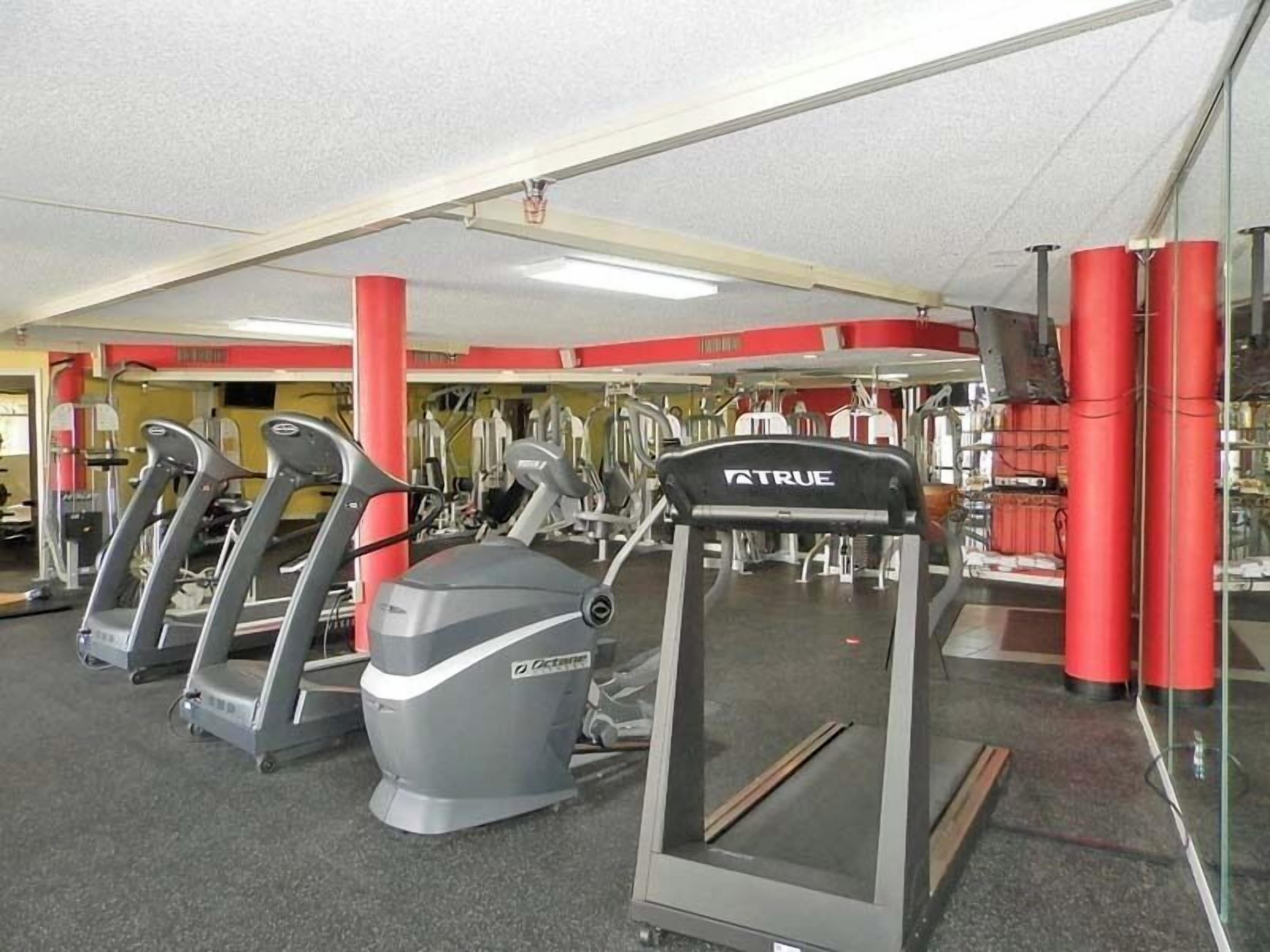 Ein Fitnessstudio mit Laufbändern, Kraftgeräten und roten Säulen.