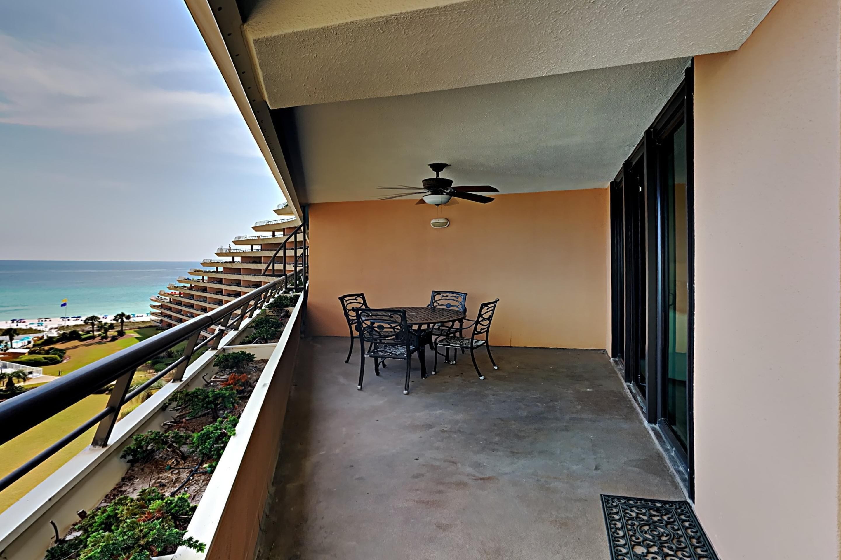 Uma varanda com mesa e cadeiras, um ventilador de teto e vista para o oceano.