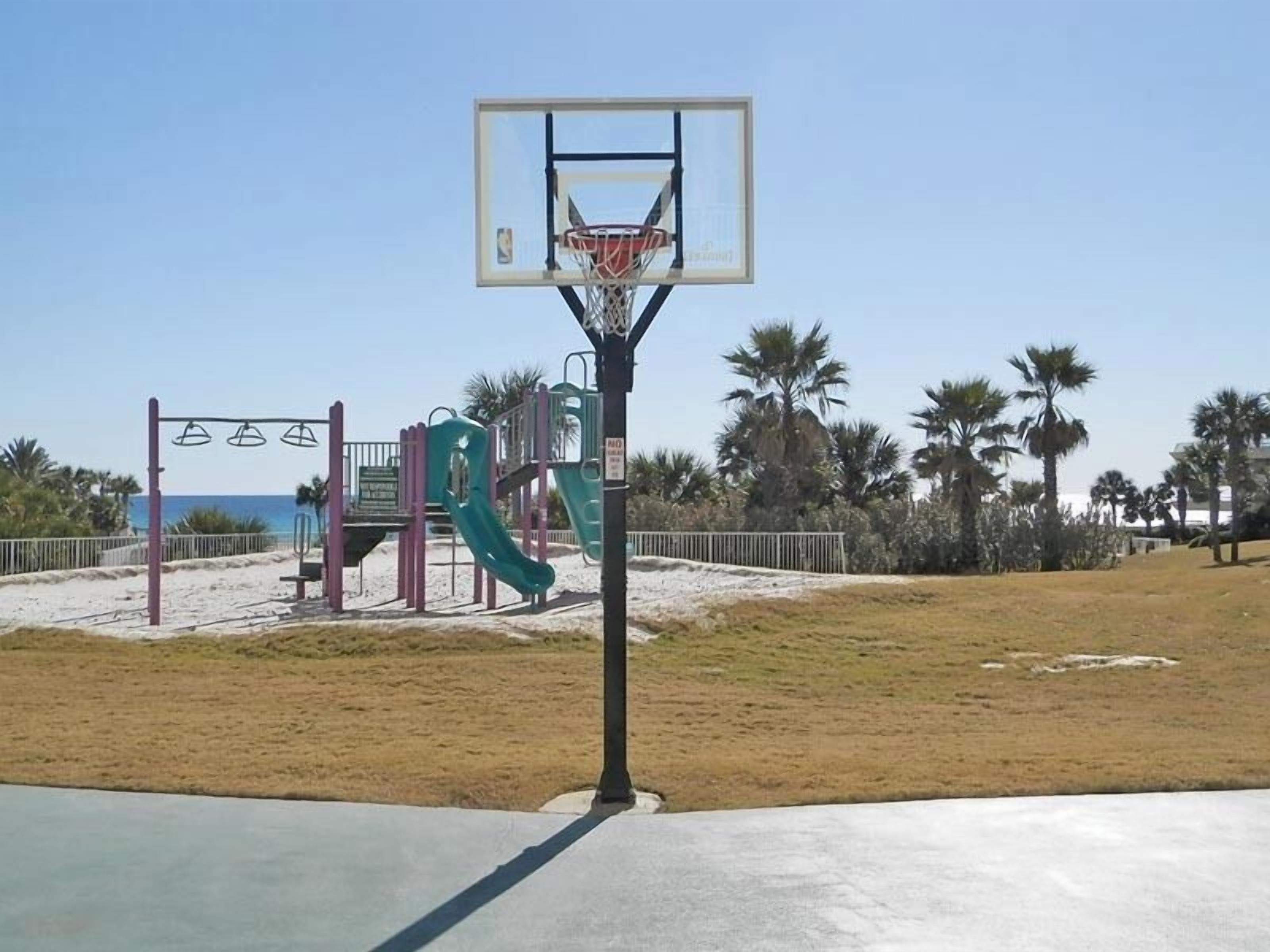 A basketball court with a hoop, a slide, and a swing set.
