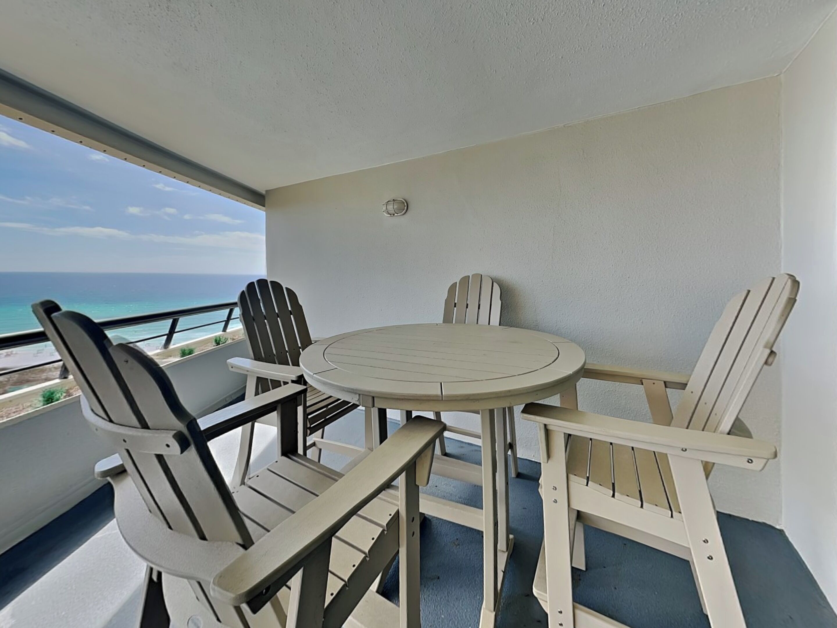 Ein Balkon mit rundem Tisch und vier Adirondack-Stühlen, mit Blick auf einen Strand.