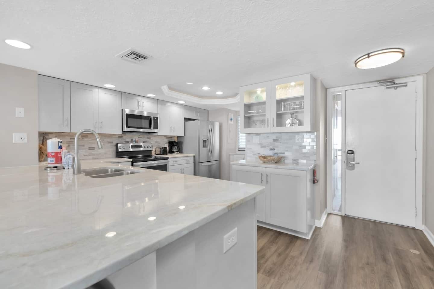 A modern kitchen with white cabinetry, stainless steel appliances, and a marble countertop.
