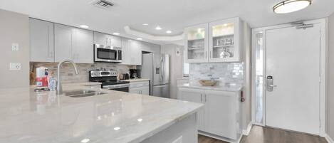 A modern kitchen with white cabinetry, stainless steel appliances, and a marble countertop.
