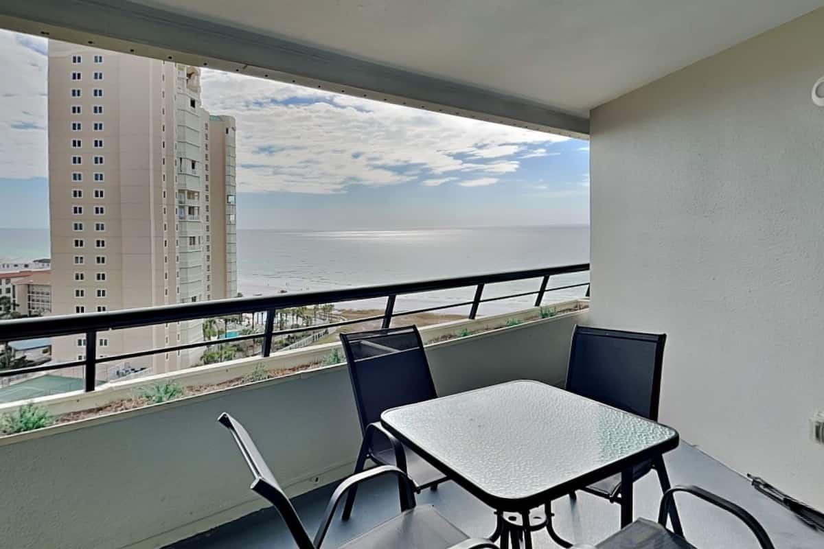 A balcony with a table and chairs, overlooking a beach and a tall building.
