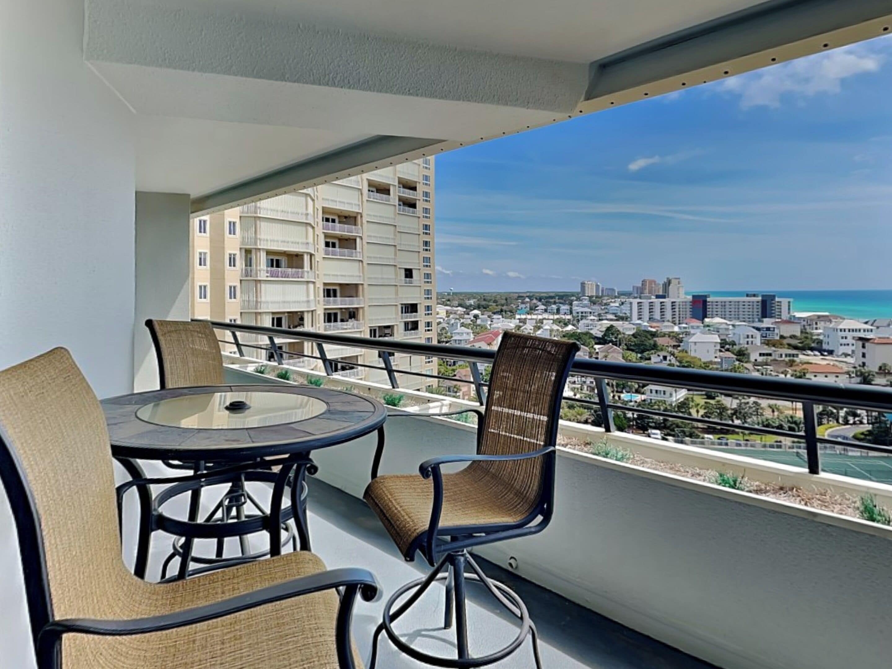 A balcony with a round table and chairs, overlooking a cityscape and the ocean.