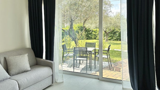 A modern living room with a grey sofa, a glass door leading to an outdoor patio with a table and chairs. - Abitatt (Fosdinovo)