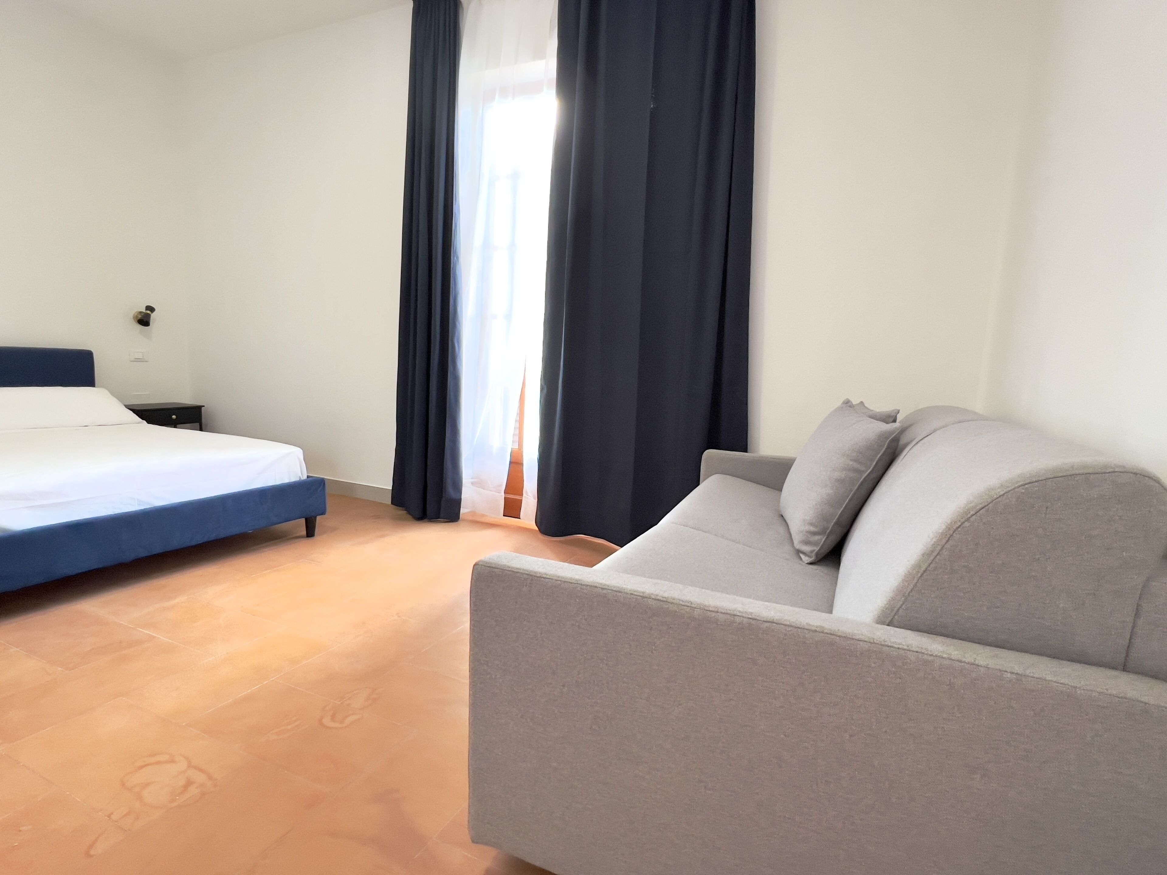 A hotel room with a bed, a sofa, a nightstand, and a window with curtains.