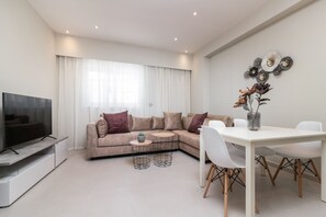 Una sala de estar moderna con un sofá seccional, un televisor de pantalla plana, una mesa de comedor con sillas y un adorno de pared.