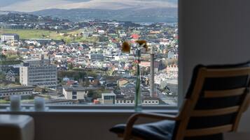 A room with a view of a cityscape through a window, a chair, and a vase with flowers.