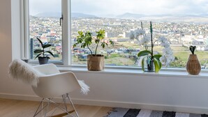 A modern room with a large window, a rocking chair, and several potted plants. - Sea & City View - Luxurious - Hiking (Argir)