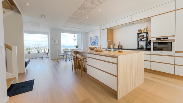 A modern kitchen with a large island, wooden flooring, and a view of the city. - Sea & City View - Luxurious - Hiking (Argir)