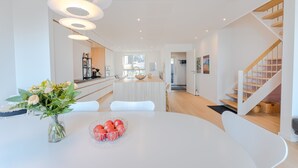 A modern kitchen with a white table, a vase with flowers, and a bowl of apples. - Sea & City View - Luxurious - Hiking (Argir)