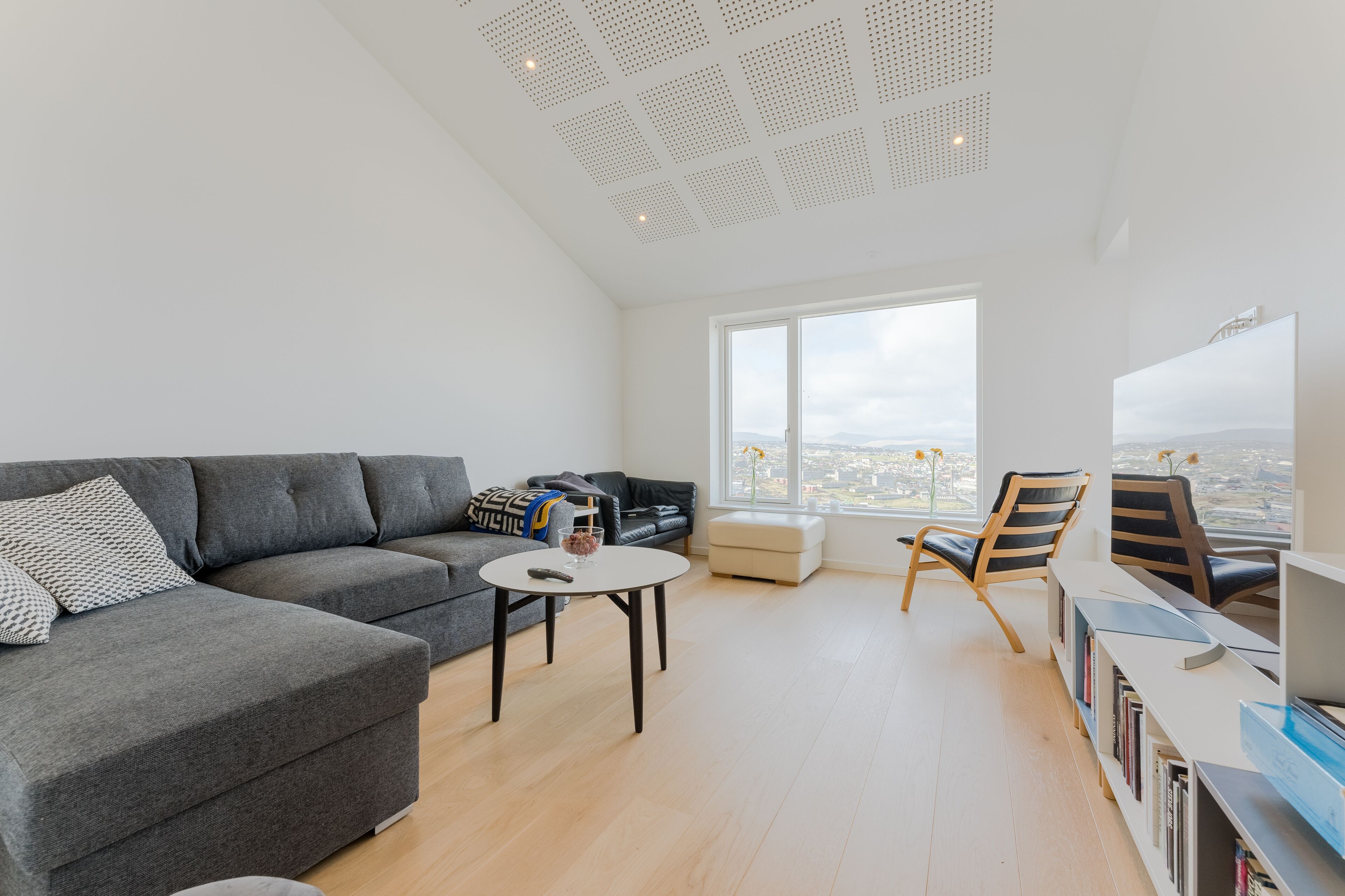 Una sala de estar moderna con un sofá seccional gris, una mesita redonda y una estantería.