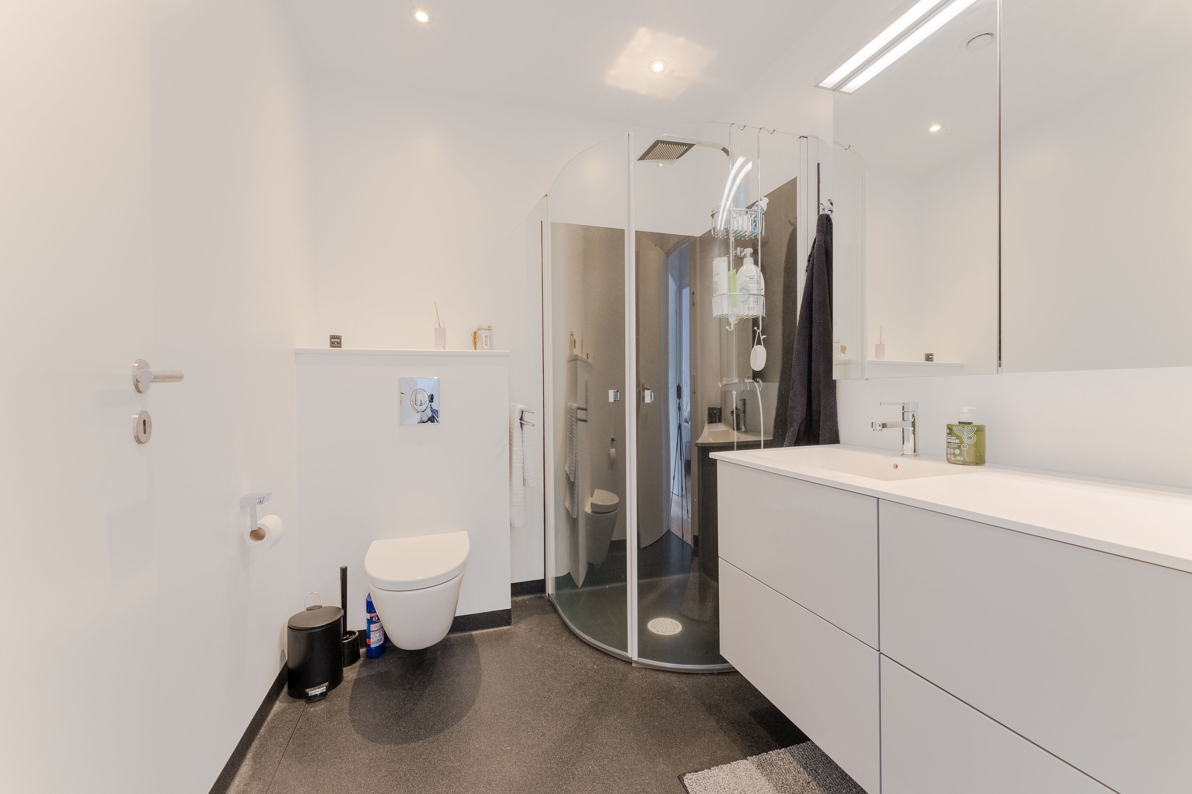 A modern bathroom with a glass-enclosed shower, a white sink, and a large mirror.