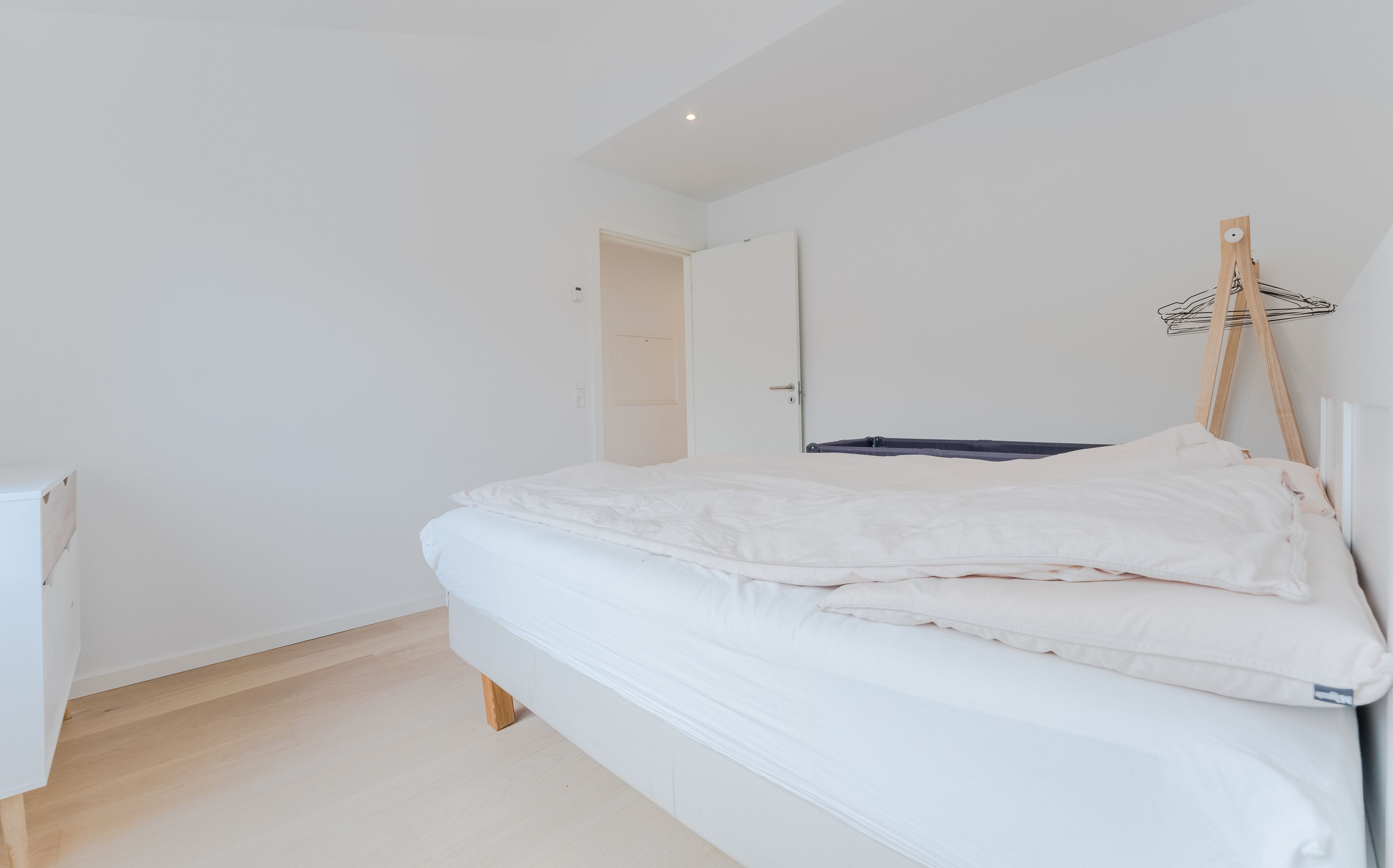 A minimalist bedroom with a single bed, a wooden floor, and a white wardrobe.