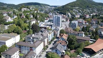 Eine Luftaufnahme einer Stadt mit einer Mischung aus Wohn- und Geschäftsgebäuden, umgeben von Hügeln und Grünflächen.