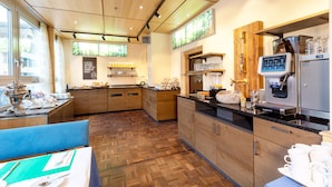 A modern kitchen with wooden cabinets, a coffee machine, and a dining area with a blue chair and table set. - Hotel Linde 24h Self Check-in (Baden)