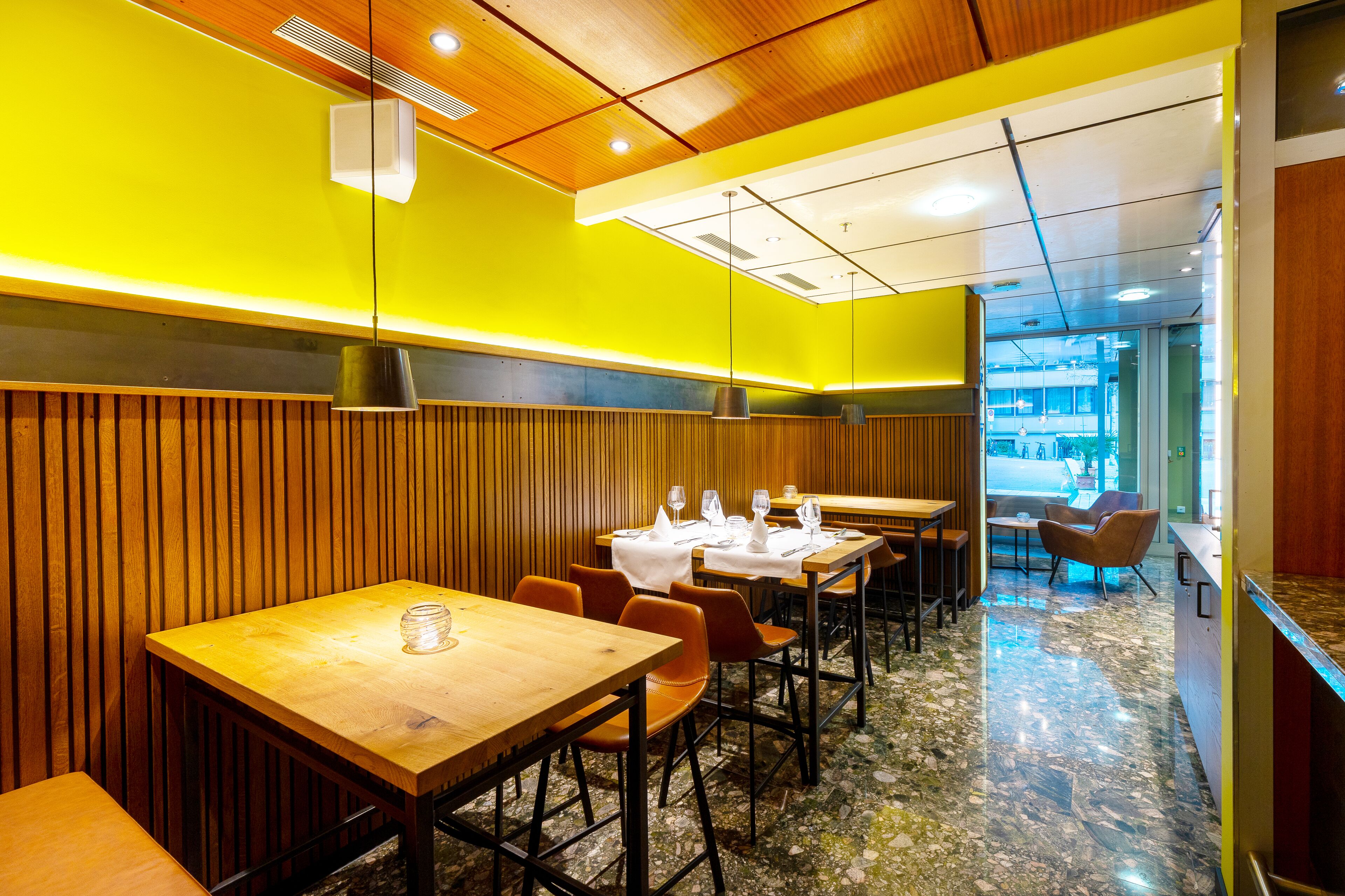 A restaurant with wooden paneling, tables set with white tablecloths, and a marble floor.
