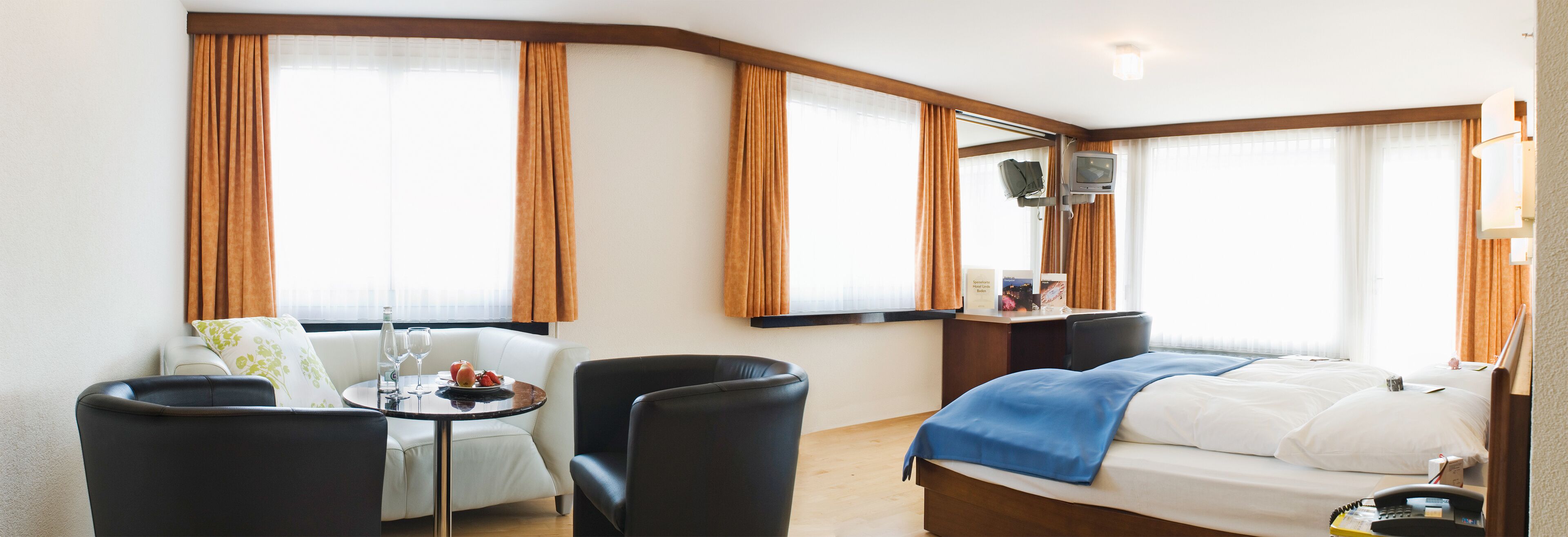 Habitación de hotel con cama, escritorio, silla, mesa con bandeja de fruta y televisión.