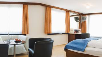 Habitación de hotel con cama, escritorio, silla, mesa con bandeja de fruta y televisión.