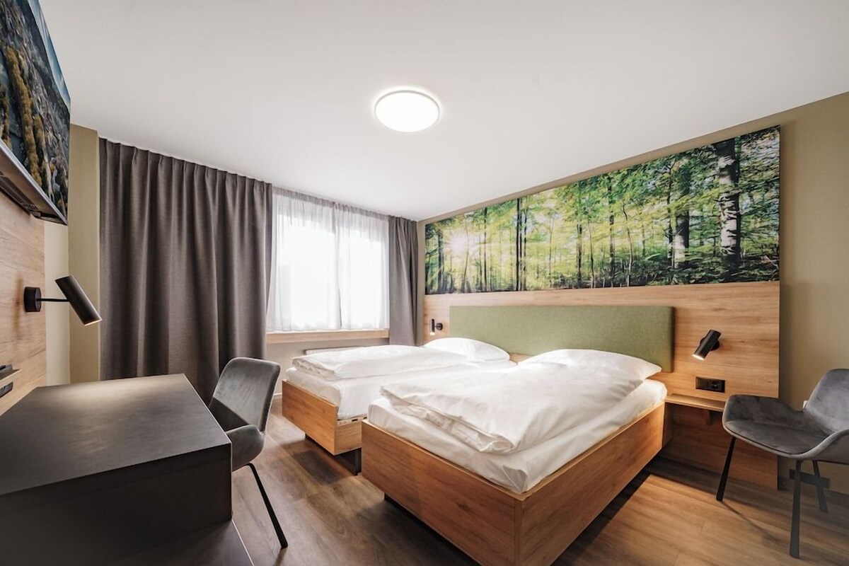 Quarto de hotel com duas camas, uma escrivaninha e uma cadeira.