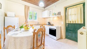Une cuisine avec une table à manger, des chaises, un réfrigérateur, un four et une porte verte.