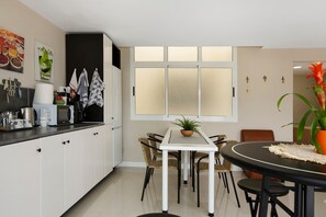 Une cuisine moderne avec des meubles blancs, une table à manger avec des chaises, une plante en pot et une fenêtre avec des panneaux de verre dépoli.