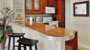 Una cocina con armarios de madera, un microondas blanco y una isla de acero inoxidable con taburetes.