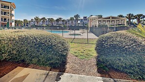 Zona de piscina con cielo despejado, rodeada de setos cuidados y un edificio de estilo arquitectónico distintivo.