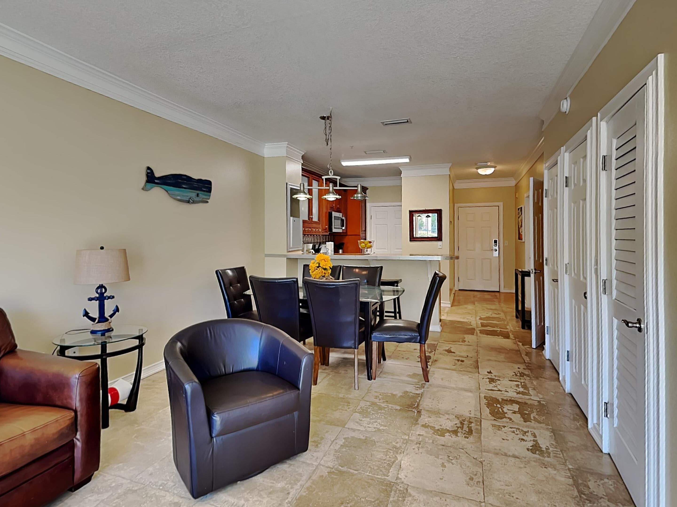 A living room with a sofa, a dining area with chairs and a table, a kitchen with cabinets and a countertop, and a hallway with doors.