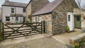 Una cabaña de piedra con un portón de madera, una puerta y un letrero que dice "Ty Gwyn Cottage".