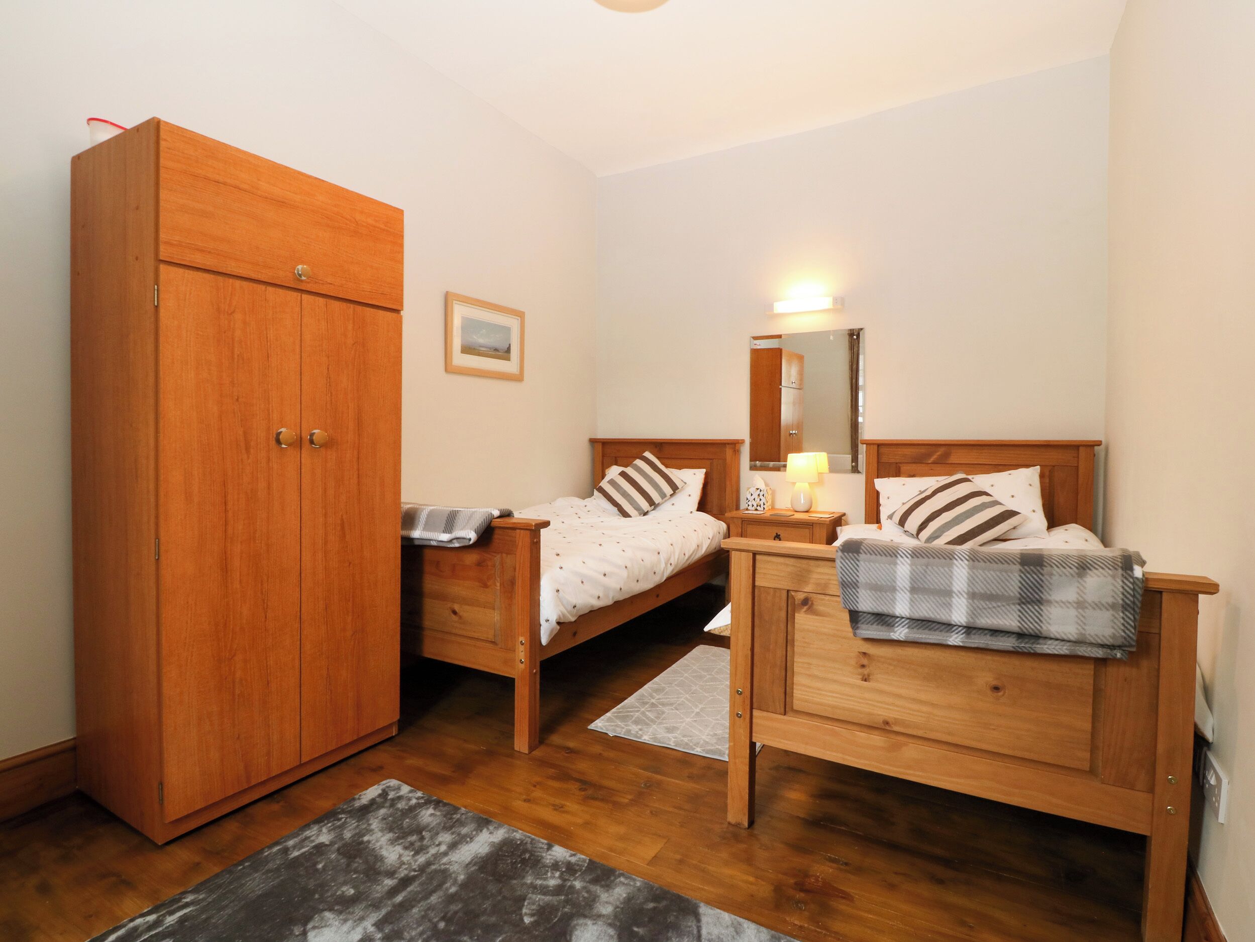 A bedroom with two wooden beds, a wardrobe, a bedside table with a lamp, and a mirror on the wall.