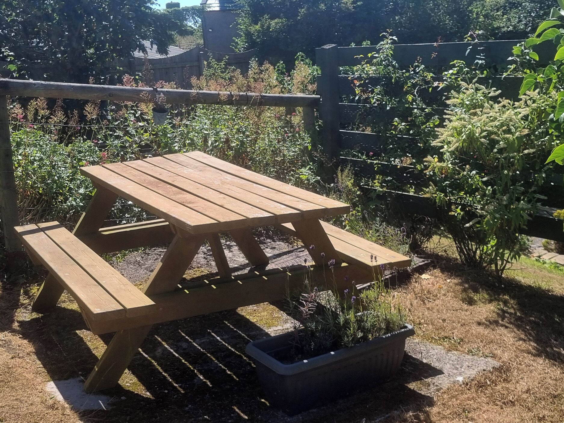 A wooden picnic table with benches in a garden setting.