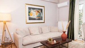 Un salon avec un canapé beige, une table basse agrémentée d’objets décoratifs, un lampadaire et un tableau abstrait encadré accroché au mur.