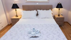 Un lit bien fait, avec du linge de lit blanc, deux tables de chevet avec des lampes, et un plateau contenant des tasses et des soucoupes blanches posé sur le lit.