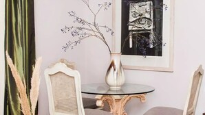 Un coin repas avec une table ronde, deux chaises, un vase contenant des plantes séchées et un tableau encadré accroché au mur.