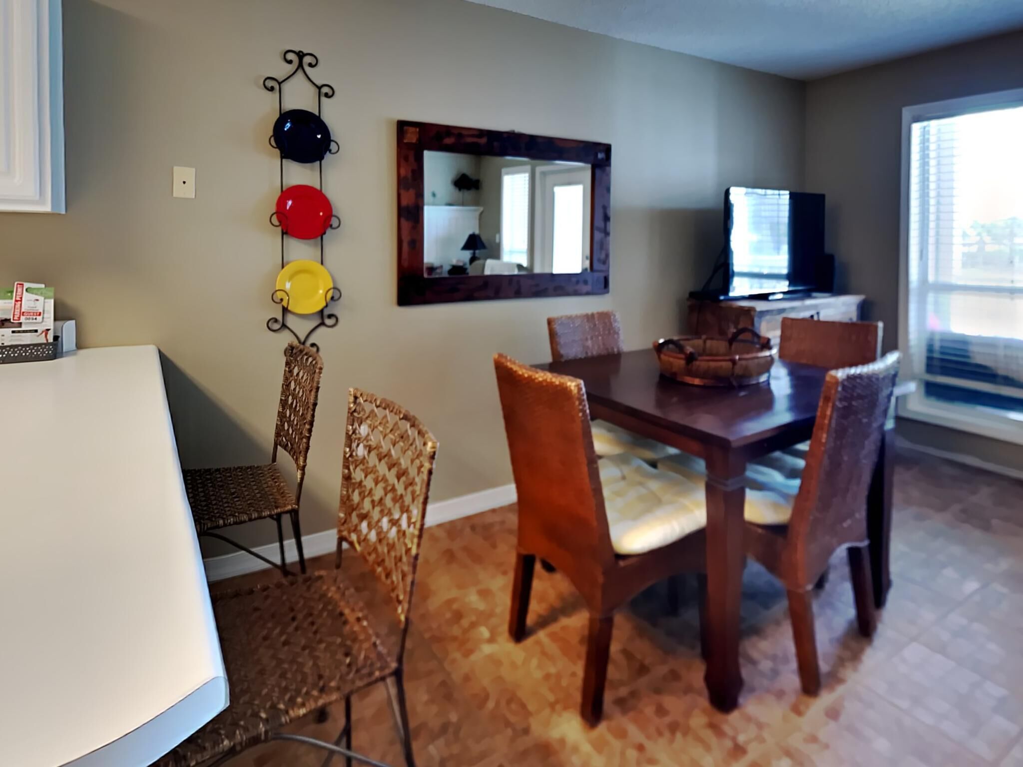 A dining area with a wooden table and chairs, a mirror on the wall, and a window with blinds.