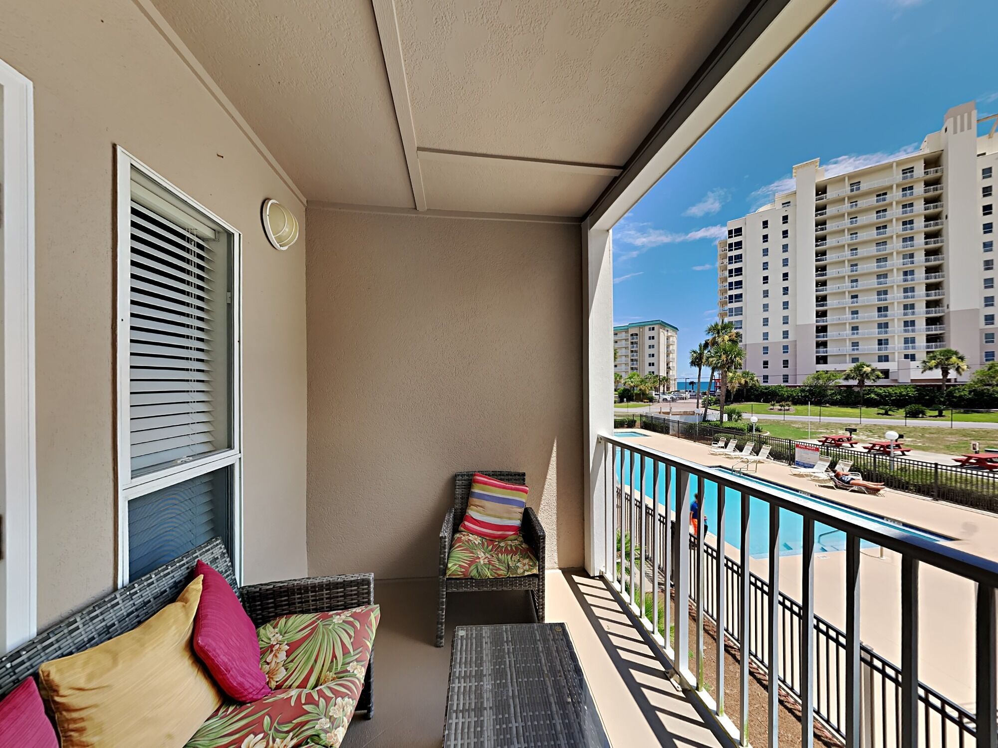 A balcony with wicker furniture, a pool, and high-rise buildings in the background.