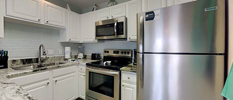 A modern kitchen with white cabinets, stainless steel appliances, a microwave, a refrigerator, and a built-in oven.