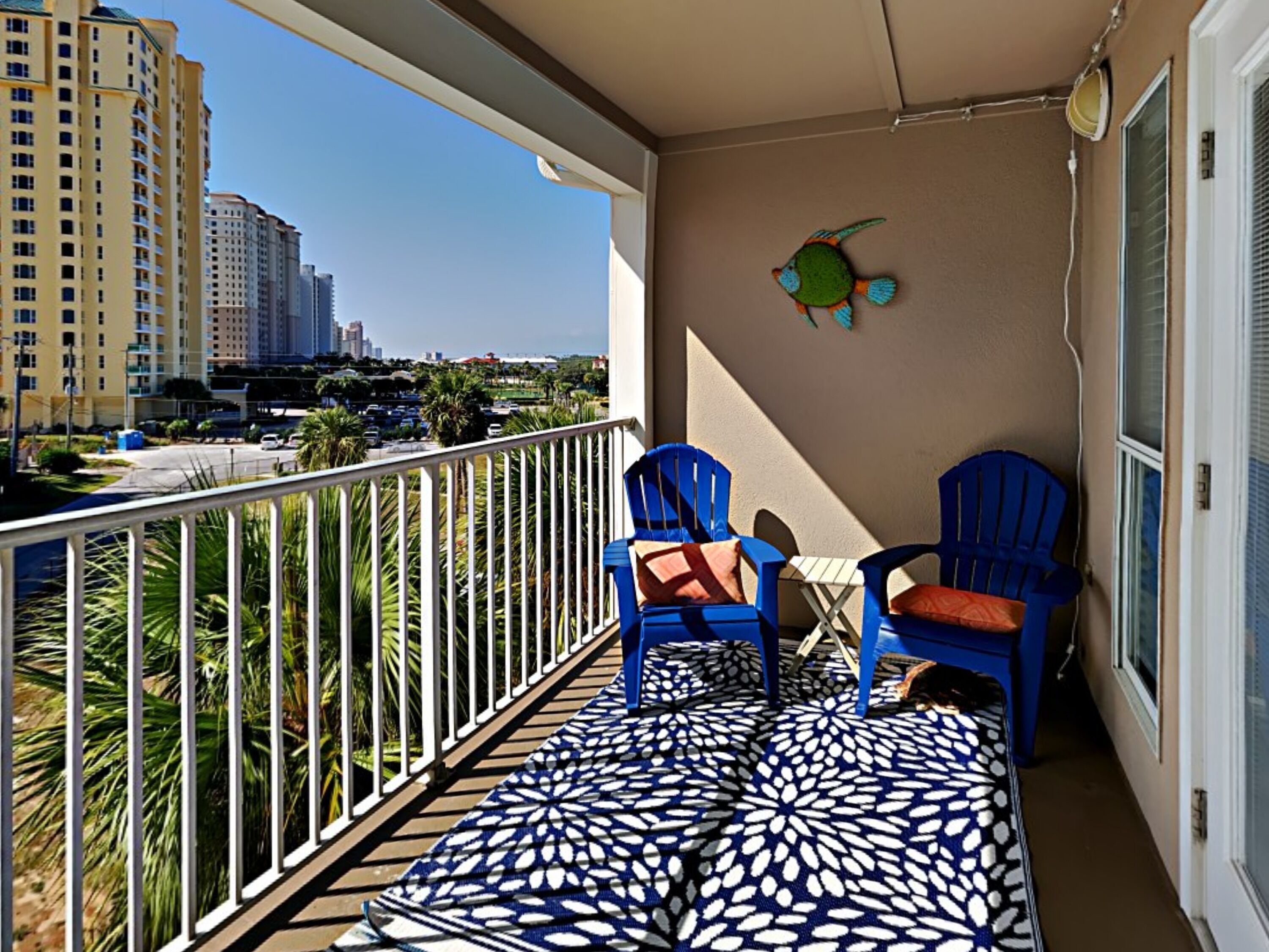 A balcony with two blue chairs, a patterned rug, and a wall decoration.