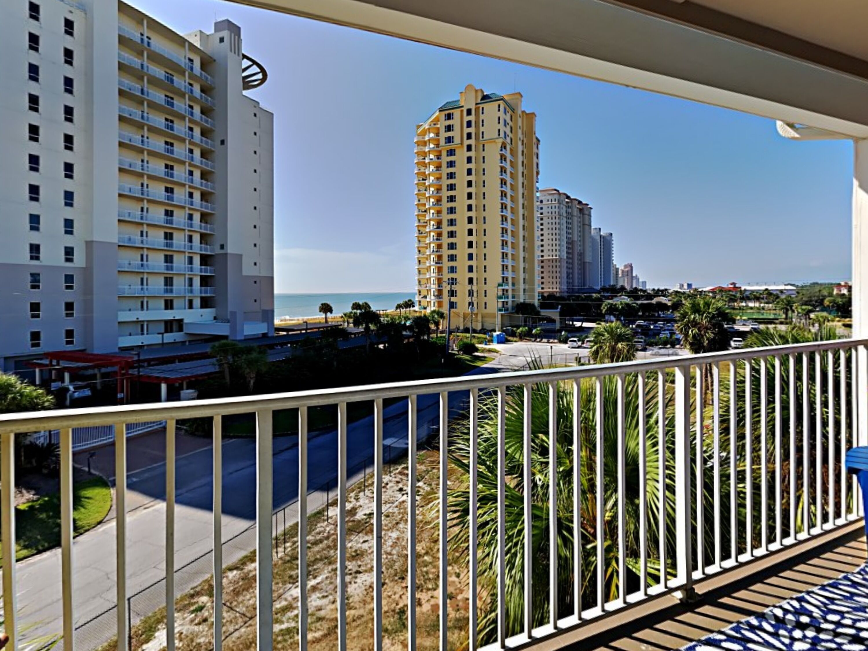 Un balcón con vista a una playa, palmeras y edificios altos.