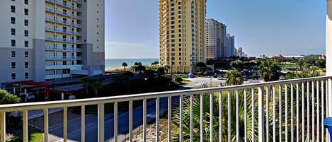 Un balcón con vista a una playa, palmeras y edificios altos.