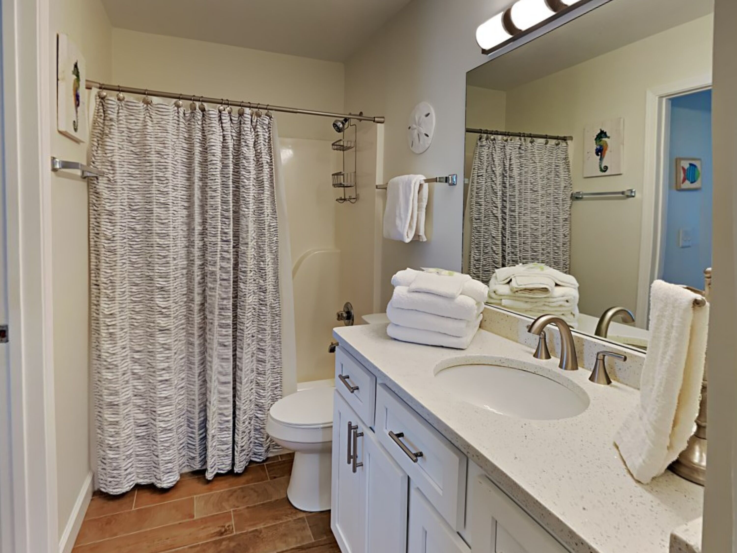 A modern bathroom with a white sink, vanity, and a large mirror. There is a shower curtain and a toilet visible.