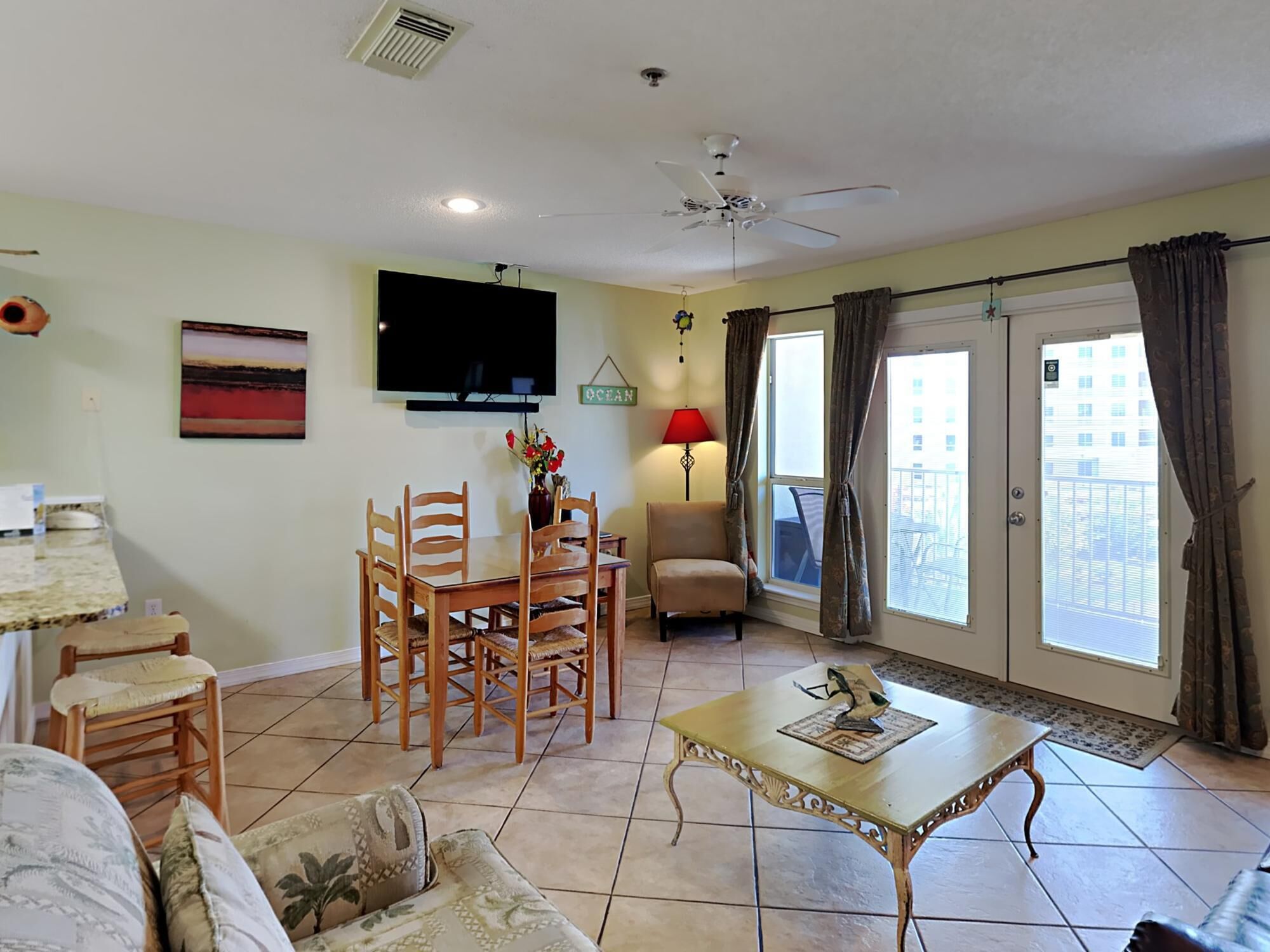 A living room with a dining table, chairs, a sofa, a TV, a lamp, and a balcony with curtains.