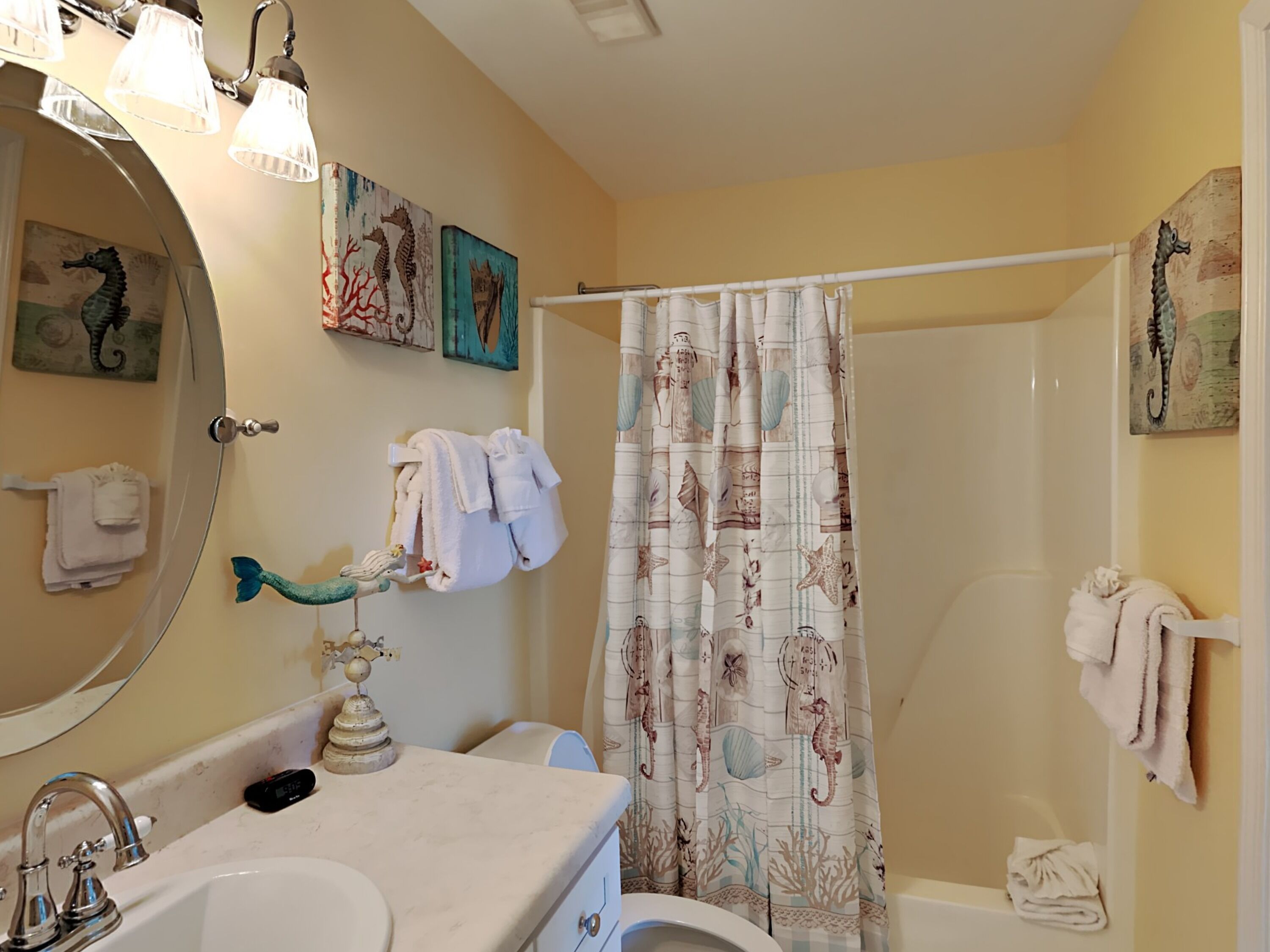 A bathroom with a bathtub, a shower curtain with seahorse designs, a sink with a mirror, and towels hanging on the wall.