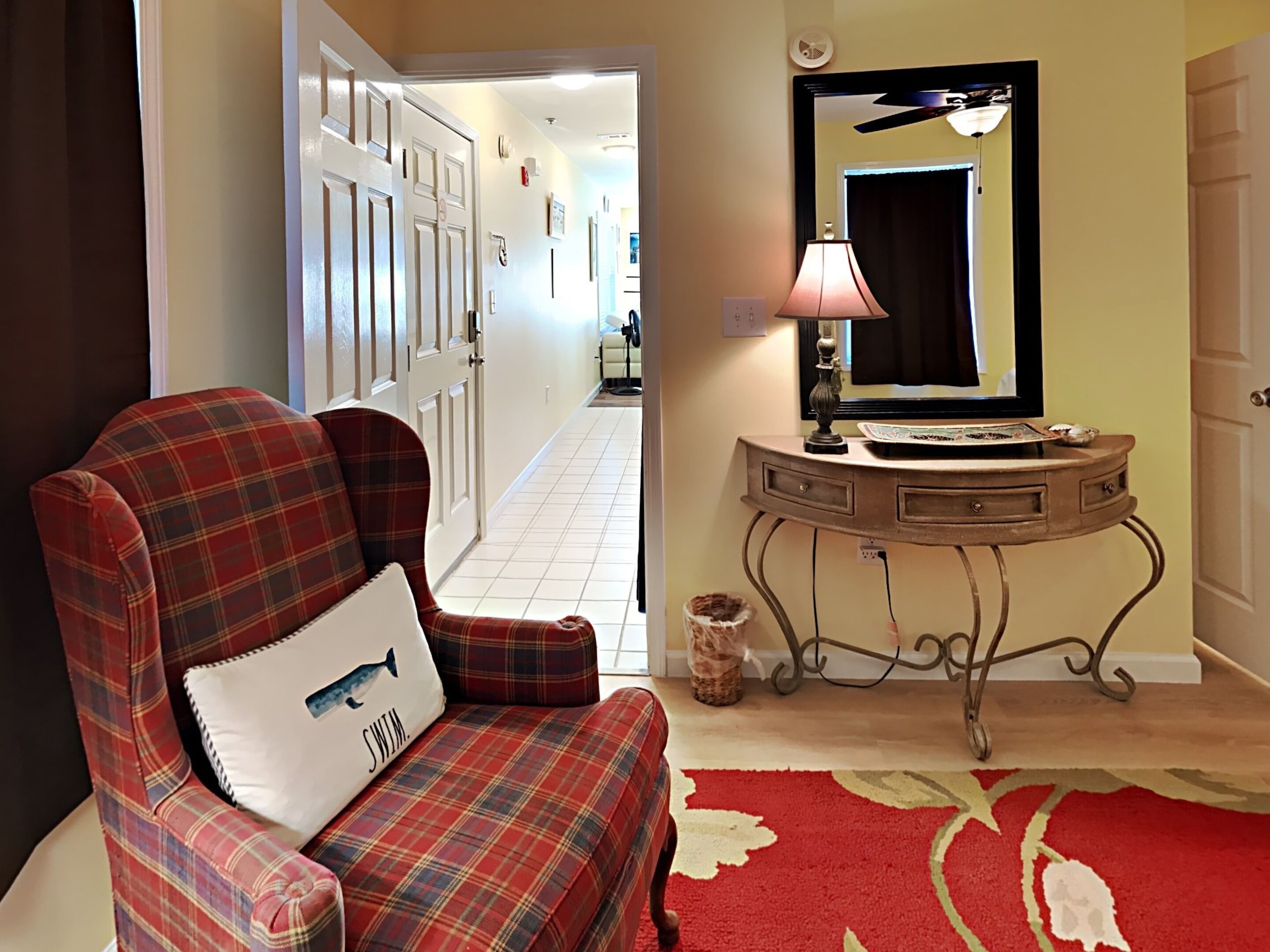A living room with a plaid sofa, a small console table with a mirror, and a red carpet.