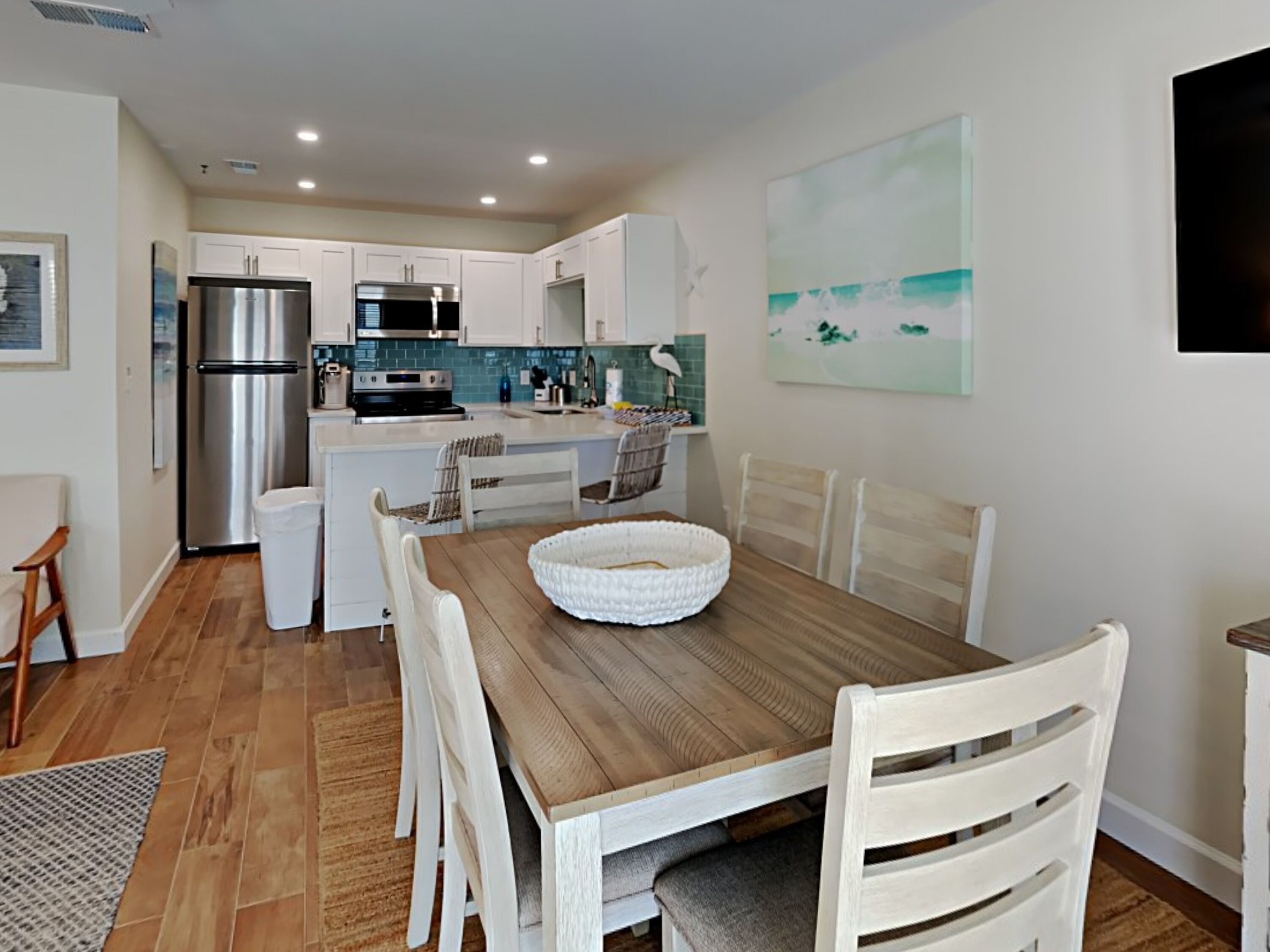 A modern kitchen with white cabinets, stainless steel appliances, and a wooden dining table with white chairs.