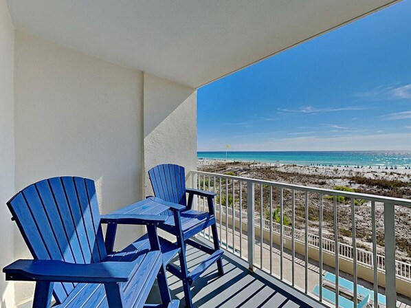 Un balcón con vista a la playa, una piscina y sillas Adirondack azules.