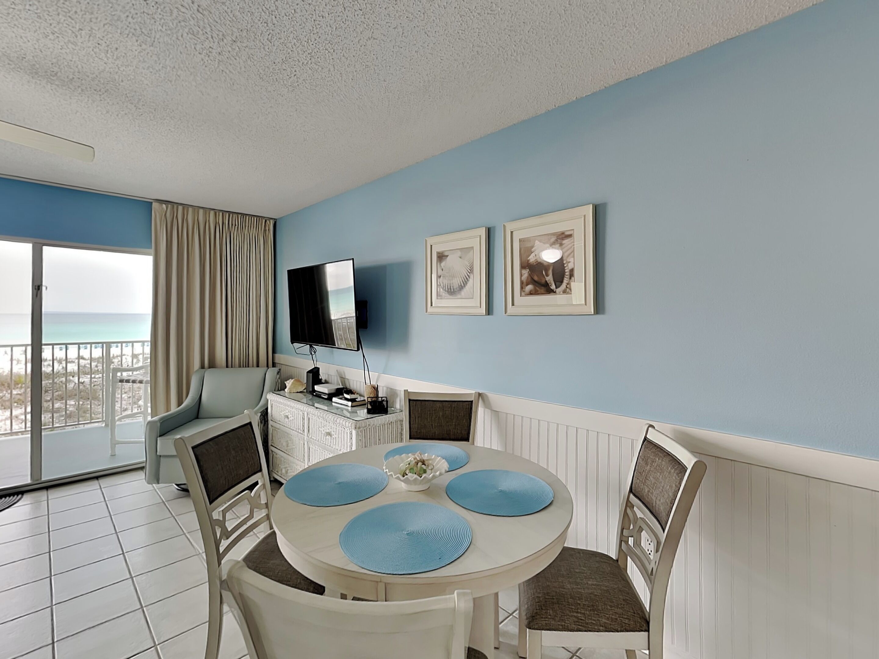 A room with a round dining table, chairs, a flat-screen TV, and framed pictures on the wall.