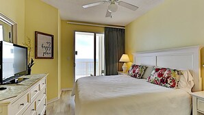 Ein Hotelzimmer mit Bett, Fernseher, Deckenventilator, Balkon mit Vorhängen und einem Schild an der Wand.